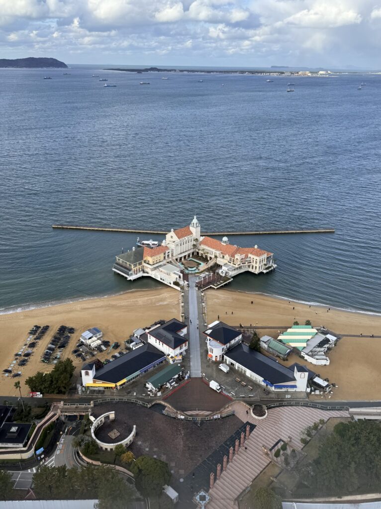 An aerial view of a beachside resort with a sandy path leading to a large, white building, surrounded by calm waters and a peaceful landscape.