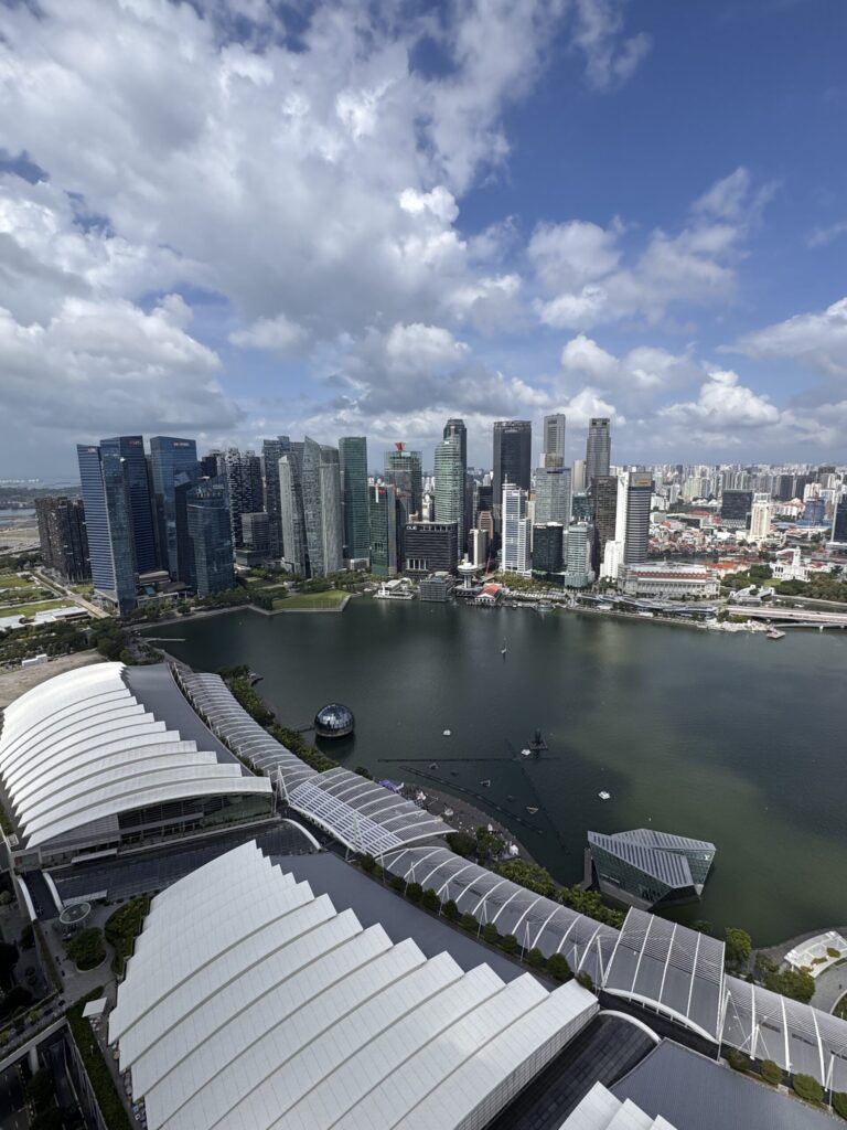 A daytime aerial view of the Marina Bay area in Singapore, showcasing the city's skyline, with modern skyscrapers surrounding a calm body of water.