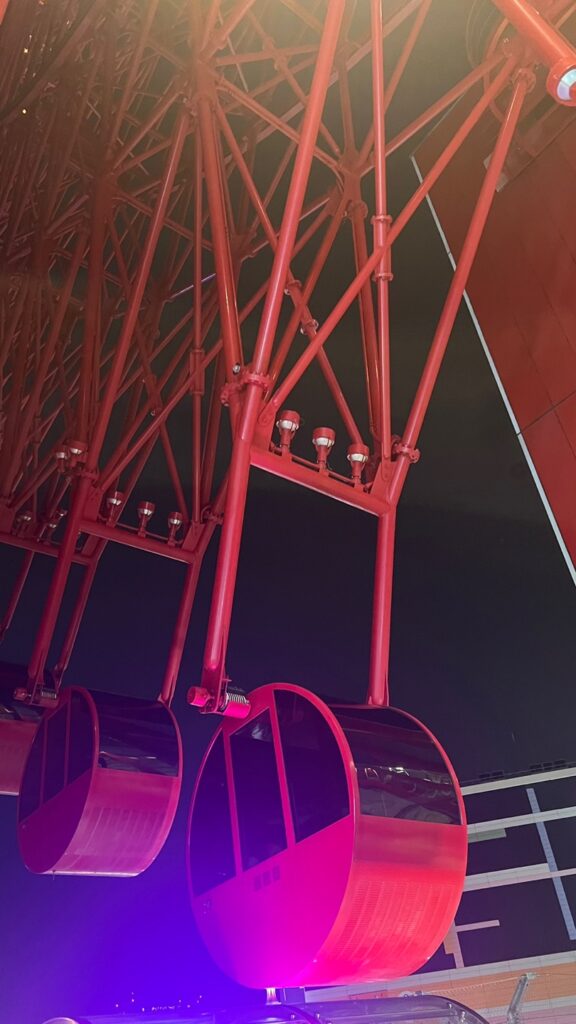 A close-up view of a red Ferris wheel with brightly lit cabins, set against the night sky.
