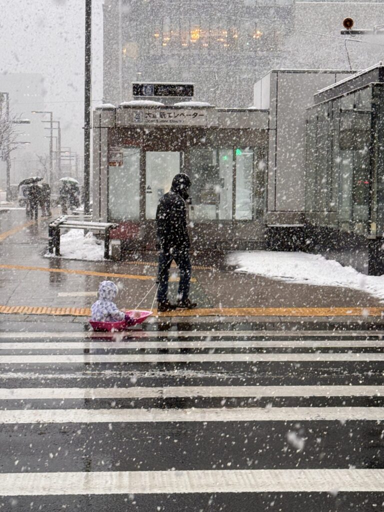 Heavy snow in Sapporo — a father pulling his child on a sled across the street.