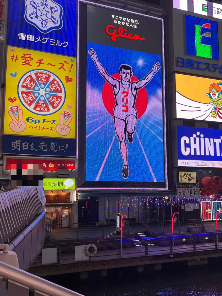 Neon signs and colorful advertisements in Dotonbori, Osaka, featuring the famous running man sign and other bright lights in the area.