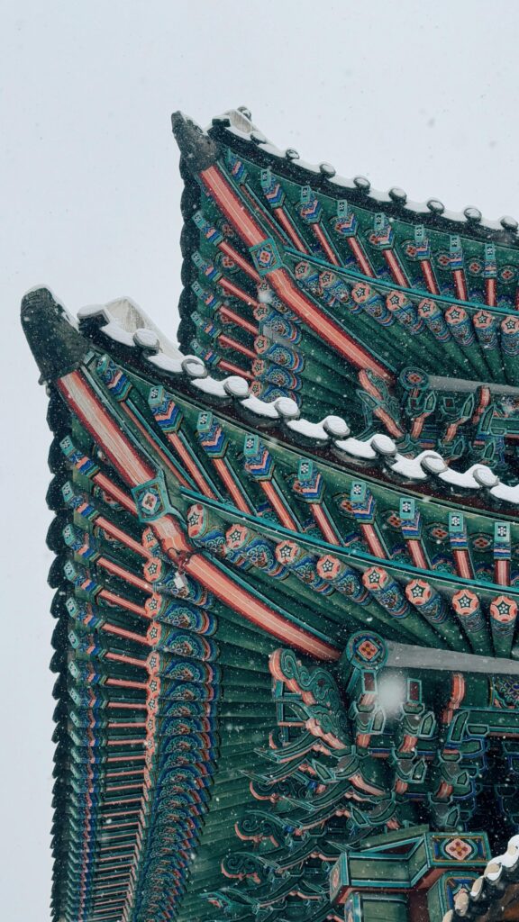 A close-up of a beautifully detailed roof of a traditional Korean building, with snow resting on the decorative eaves.