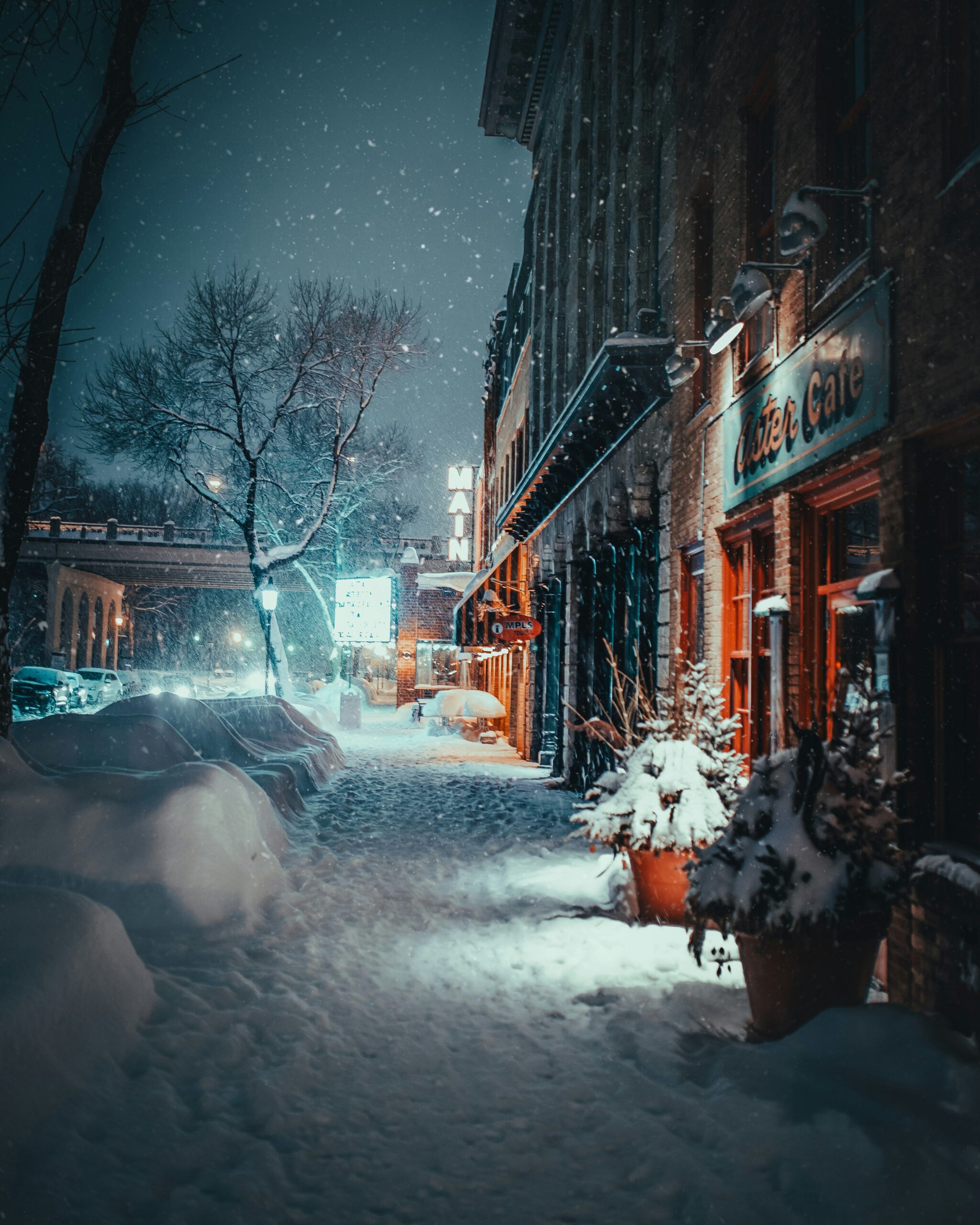 A quiet snowy street at night illuminated by warm lights from a cozy café — a gentle warmth in the cold winter air. 따뜻한 카페 불빛이 비추는 겨울밤의 고요한 눈 내리는 거리 — 차가움 속의 잔잔한 온기.