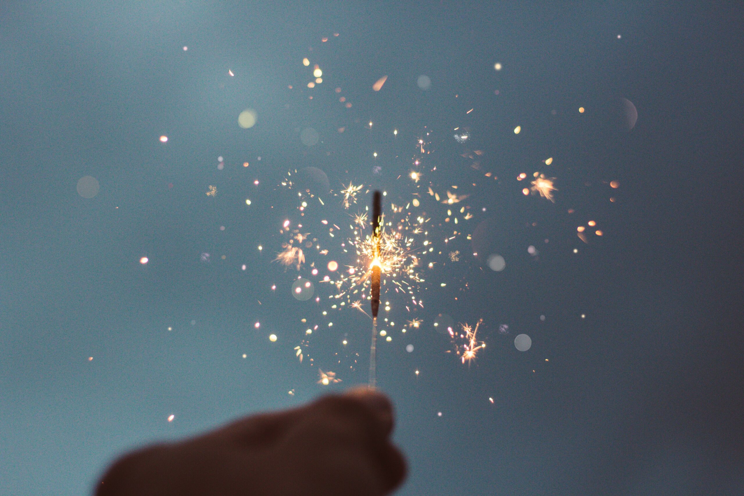 KR 연말 밤, 손에 쥔 스파클러가 어두운 하늘 속에서 잠시 빛나고 있다. EN A hand holding a sparkler glowing briefly against the dark year-end sky.