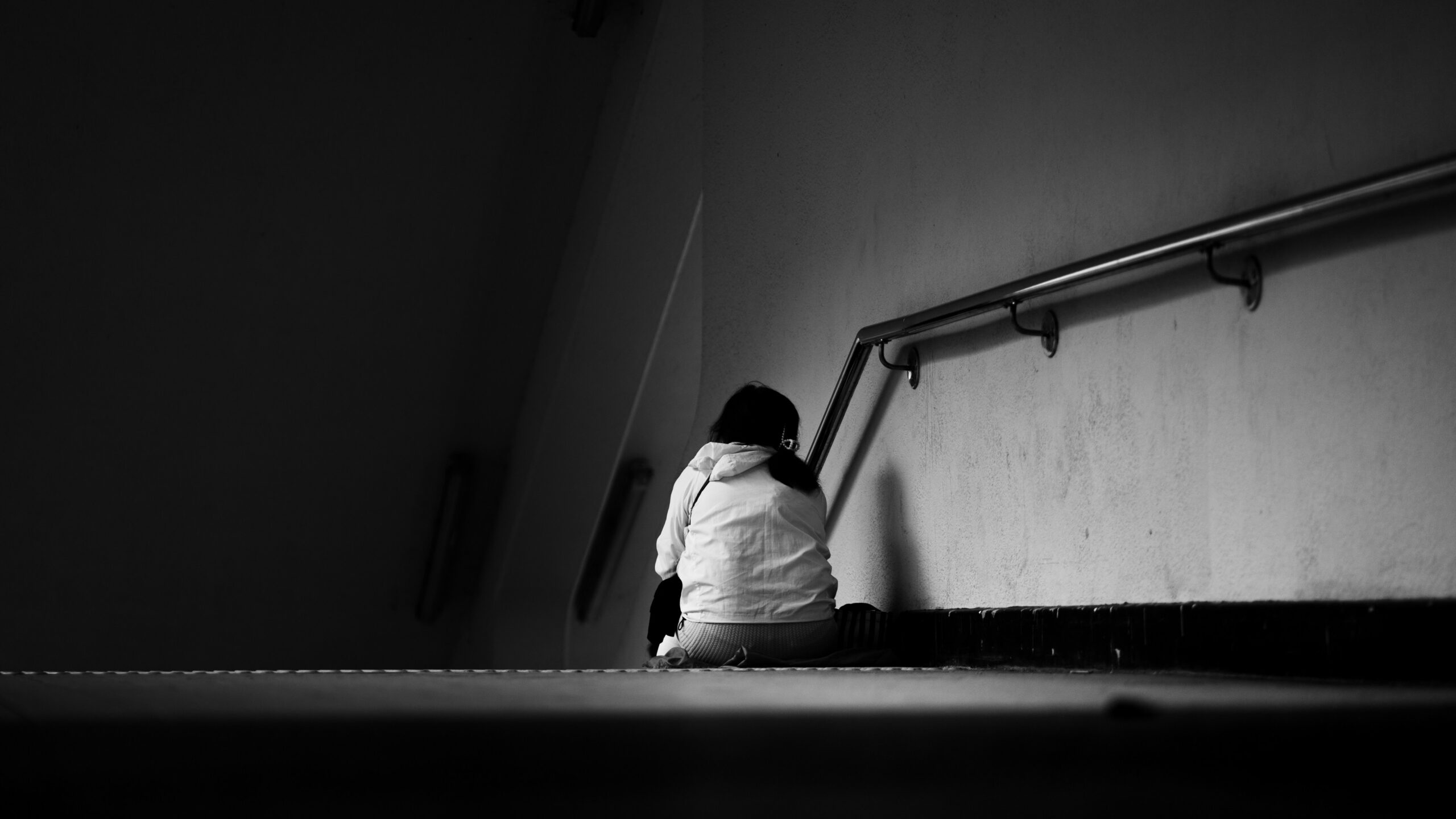 KR 계단 아래에 앉아 등을 보이고 있는 한 사람의 흑백 사진 EN A black-and-white photo of a person sitting at the bottom of a staircase, facing away